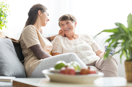 Woman talking with happy elderly mother while sitting on sofa at home during meeting