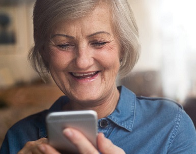 senior woman with grey hair and a blue polo shirt looking at her cell phone smiling
