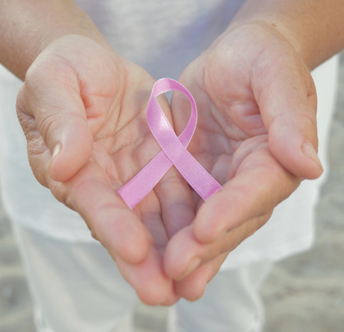 close up of a womans hands holding a pink breast cancer ribbon