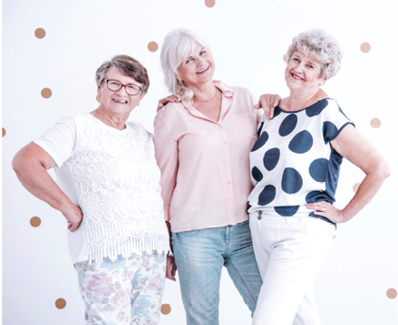 three senior women standing in front of white backdrop smiling for photo