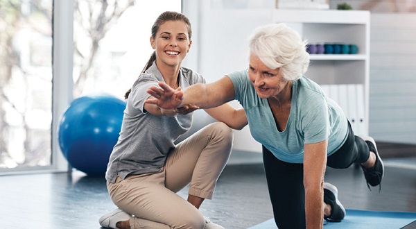 physical therapist helping older adult woman balance in yoga pose