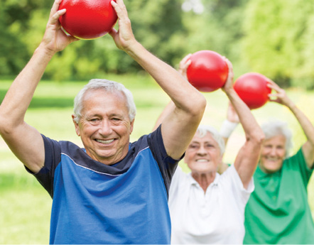 senior folks in the park exercising. Holding red weighted exercise balls.