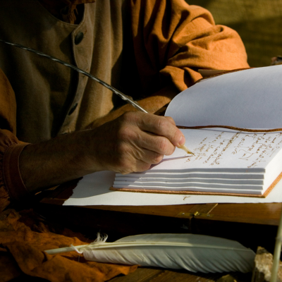 Portrait of man's arm writing in blank book using feather pen.